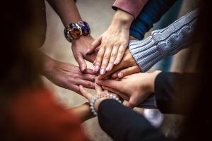 Group of people placing hands together to represent peer support, community, and accountability in addiction recovery.