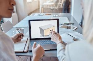 Two design engineers review plans while one points to a detailed 3D commercial structure model on a laptop