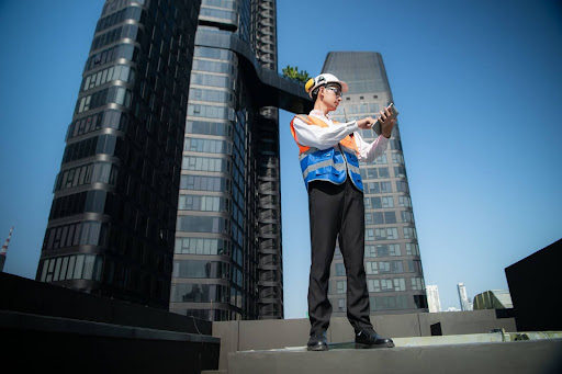An engineer reviewing live 3D scanning data on a tablet while documenting a building from the rooftop