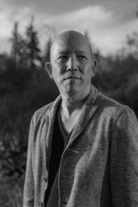 A black and white photograph of Scott Kurashige -- he stands outdoors and looks reflectively off to the left.