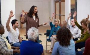 A group of adults sitting in a circle raising their hands.