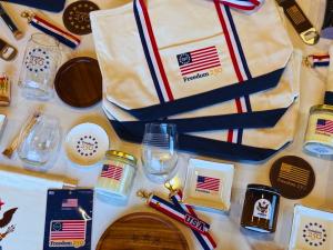 Flat lay of Thankful Greetings Freedom 250 commemorative products including canvas tote bag, candles, glassware, trays, and patriotic accessories.