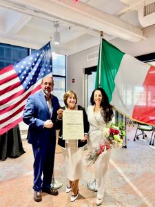 Franca Grispino with her children holding her Cavaliere certificate, the American and Italian Flags behind them in the consulate's office