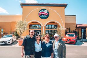 Italian family, mom, dad, grown son and daughter in front of yellow building, blue skies