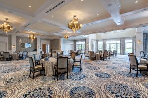 Elegant ballroom with coffered ceilings, gold chandeliers, and round tables set for dining, featuring patterned blue-and-cream carpet and large windows letting in natural light.