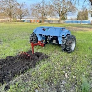 The e2T (electric two-wheel tractor) is a small, blue, tractor working in a field. The e2T tractor is using a potato digger attachment.