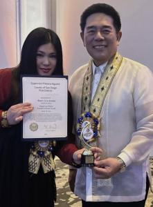 Award-winning children's author Mona Liza Santos holding the Dangal ng Pilipino Founders Citation Award certificate with Consul Adelio Angelito S. Cruz at a Filipino community recognition event in San Diego, California.