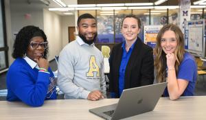 ASU Graduate Students in Library smiling surrounding a laptop.