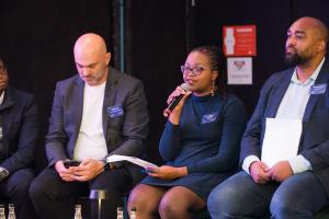 Ayanda Vabaza-Mvandaba sits alongside panelists at Startup Of The Year event speaking into the microphone.