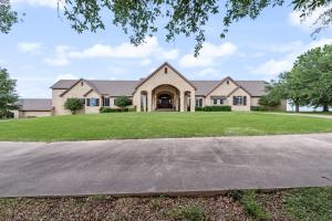 Front view of Hartlee Field Ranch with a large stone villa, grand arched entrance, expansive green lawn, circular driveway, blue sky, and tree branches framing the property.