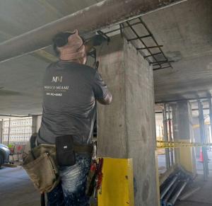 A Mersco Miami crew member restoring a structural column with the rebar cage exposed, caution tape