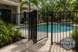 Black aluminum pool fence with an open self-closing gate surrounding a Louisiana backyard swimming pool