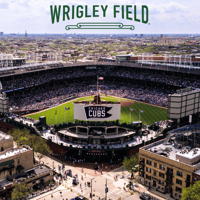 Aerial view of Wrigley Field baseball stadium filled with fans during a Chicago Cubs game, surrounded by urban buildings.