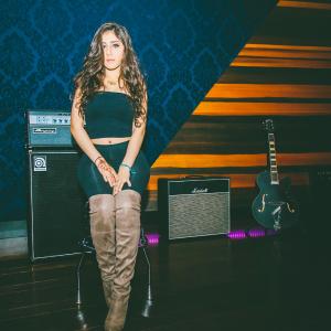 Farrah Mechael posing in a professional recording studio surrounded by musical instruments and recording equipment.