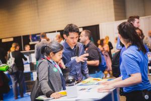 Two attendees speak with a representative across an exhibitor table on the Small Business Expo show floor.