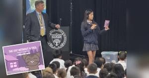 Lerraina Mak holds up her book while speaking to a Fairmont Schools assembly, with The Cat Without a Tail cover inset.