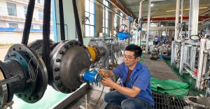 Technician in a blue work shirt adjusting the transmitter on a large flanged oval gear flow meter in an industrial workshop