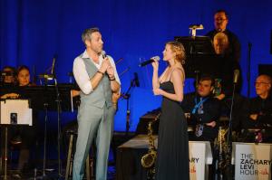 Zachary Levi and Rumer Willis sing a duet on stage during the Music is Medicine concert, looking at each other while performing the duet I See the Light from Tangled