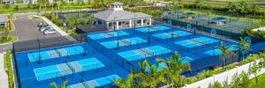A panoramic view of the outdoor pickleball facilities at Valencia Grand in Boynton Beach, showcasing a series of pristine blue courts with vibrant green accents, fully equipped for the community's active residents. Surrounded by lush landscaping and palm 