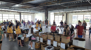 children, community organizations, and volunteers working together to assemble and pack hundreds of backpacks in a well-orchestrated assembly line
