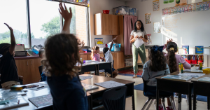 An elementary classroom at McKenzie Elementary where several students raise their hands while the teacher leads a lesson at the front of the room.