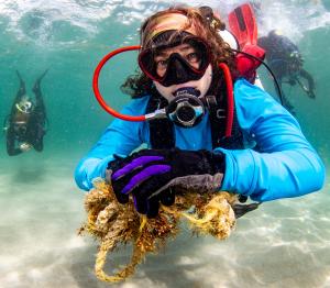 A close-up photo of founder Autumn Blum underwater in dive gear. She is holding some discarded rope as she is participating in an ocean cleanup. There are two divers behind her on either side in the background.