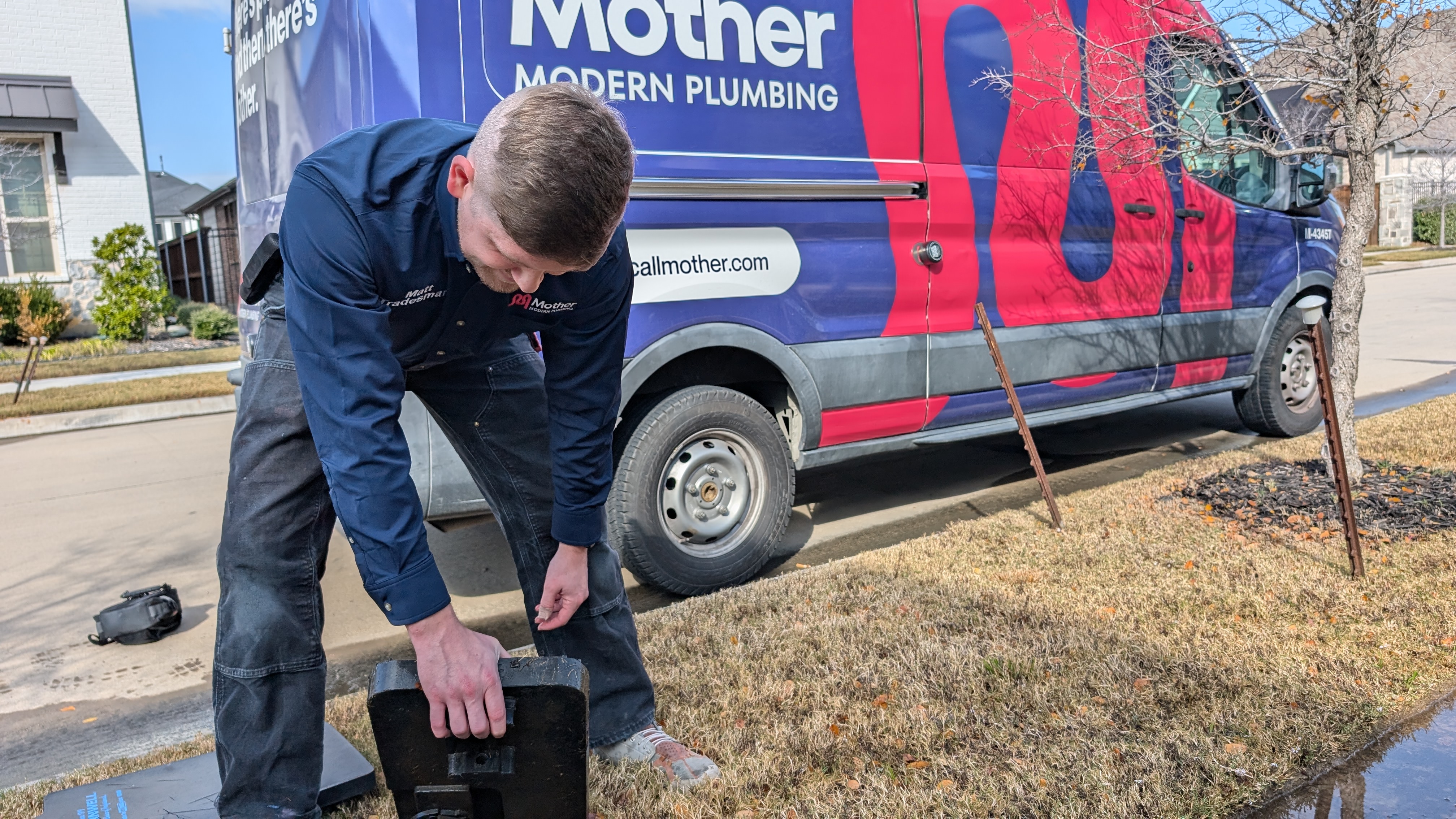 Mother modern plumbing team member standing in front of the plumbing truck opening a water meter box to locate a leak.