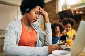Photo of a stressed parent at a computer with kids in the background