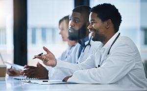 Smiling Black healthcare professionals in lab coats engaged in a discussion at a conference table, symbolizing leadership and representation in pharma.