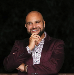 Image of REIF Founder & CEO, David Chehade smiling charismatically wearing a maroon suit jacket with white and maroon button up shirt underneath
