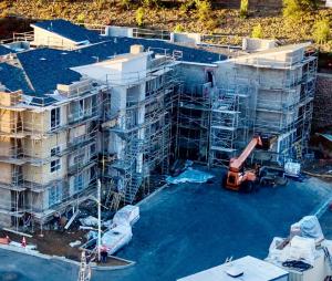 Aerial view of the La Costa Family Apartments construction site in Carlsbad, showing a multi-story building surrounded by scaffolding, workers’ materials on the ground, and a lift vehicle positioned in front as exterior construction progresses.